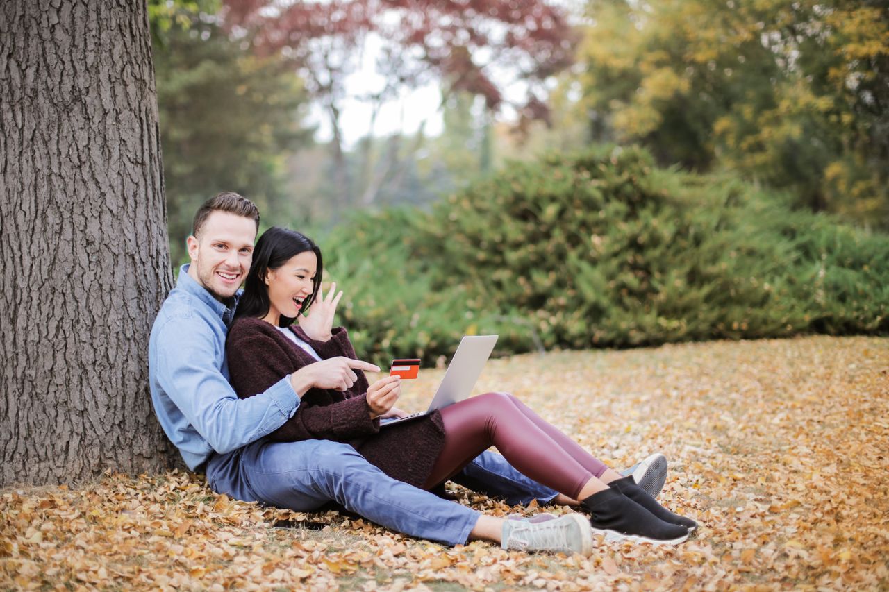 hero-img A joyful couple using a laptop and credit card outdoors during fall.
